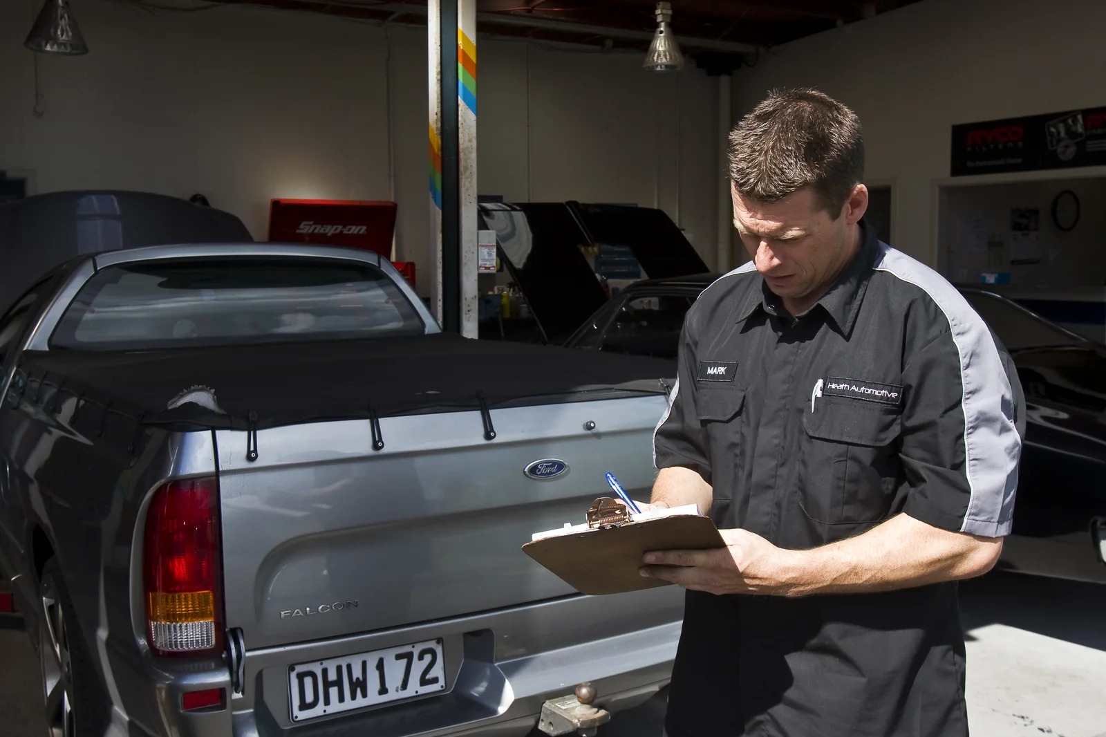 Technician writing on a clipboard beside a Falcon ute